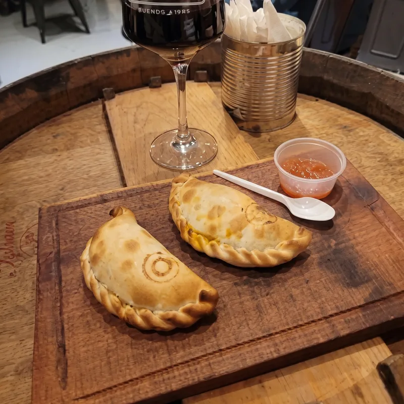 Empanadas sobre una tabla en la mesa barril, con una copa de Che Malbec