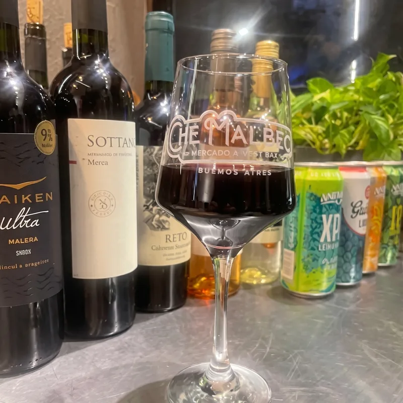 Copa de Che Malbec junto a botellas de vino argentino